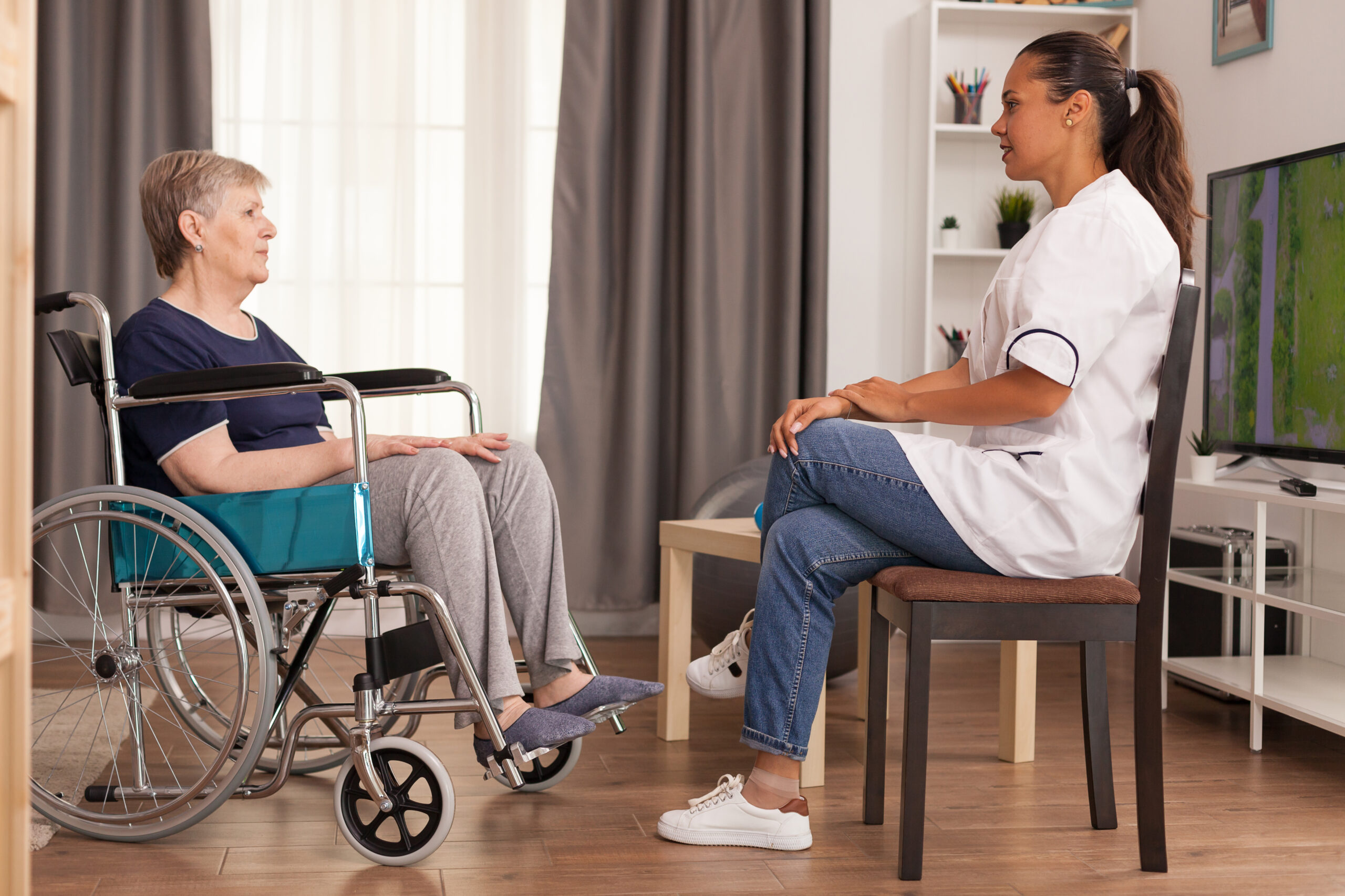 Caregiver talking with a disabled woman sitting in wheelchair. Disabled handicapped old person recovering professional help nurse, nursing retirement home treatment and rehabilitation